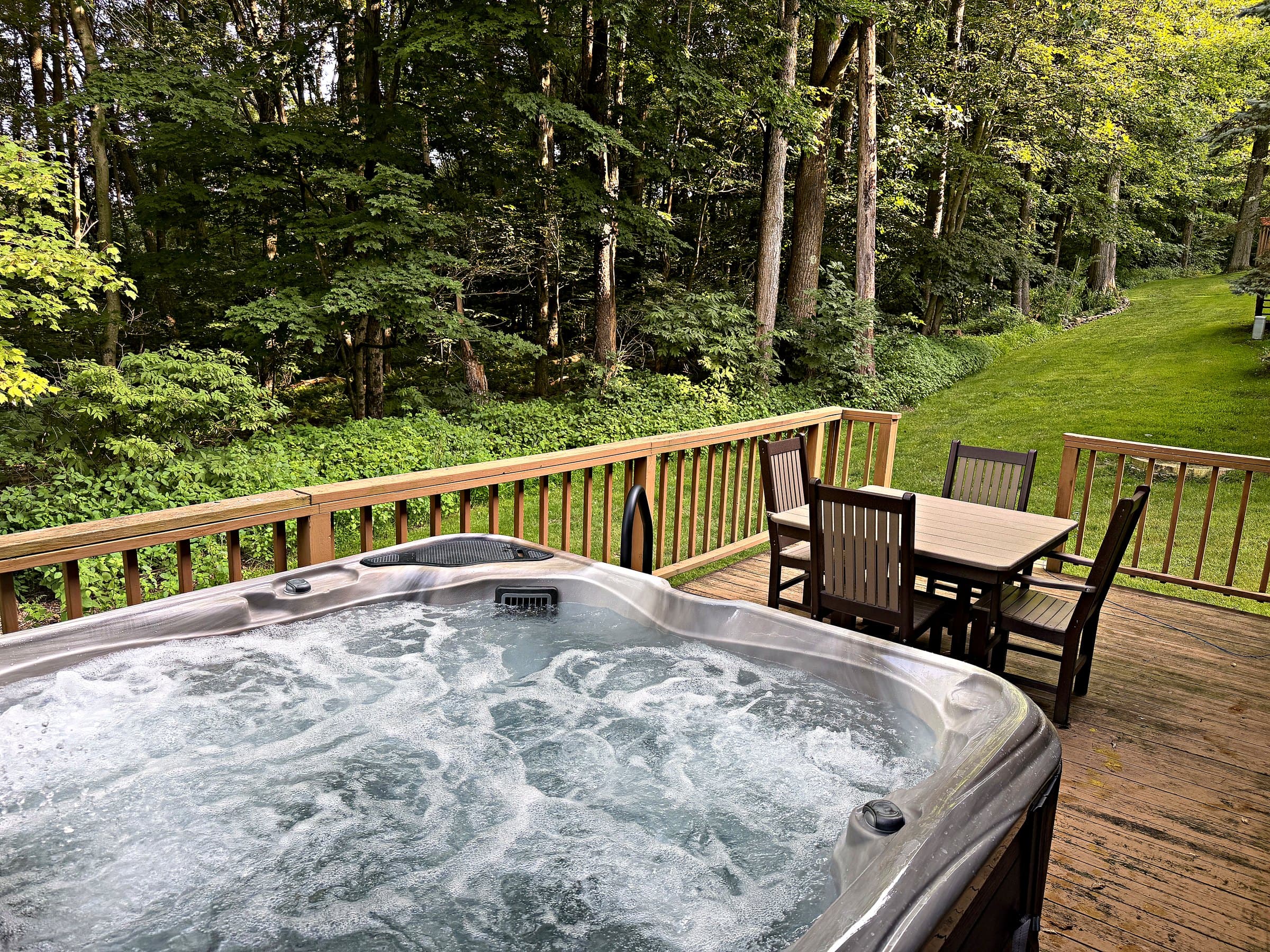 Private hot tub bubbling on the deck, with group dining and Laurel Highlands woods beyond
