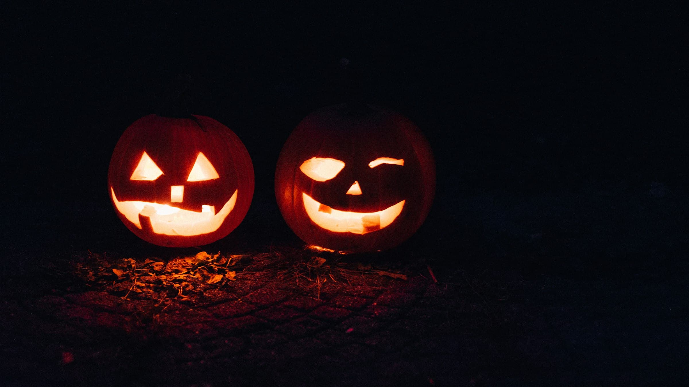 Two carved jack-o’-lanterns glowing in the dark on a leaf-strewn stone path