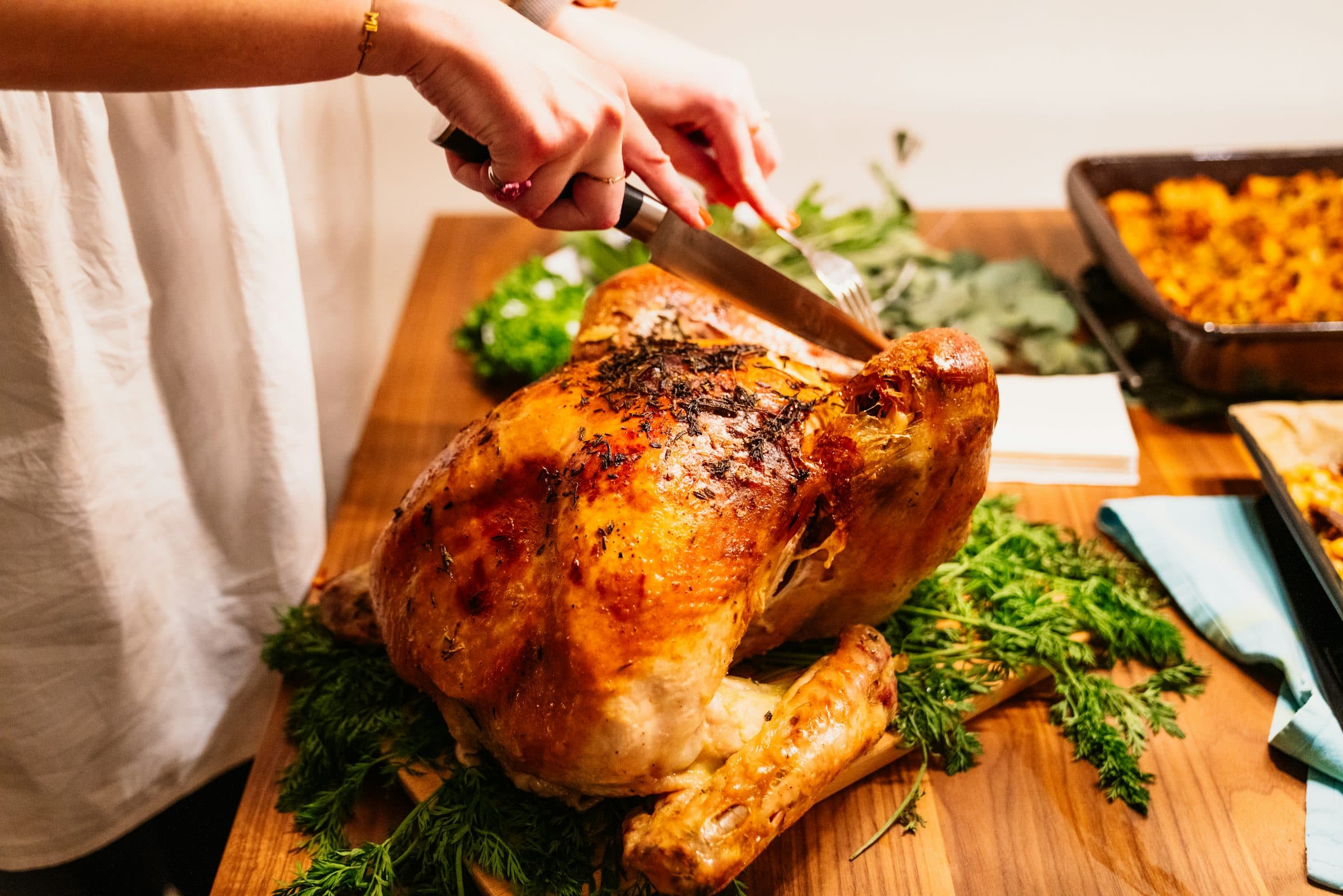 A roast turkey being carved on a wooden board beside a pan of stuffing