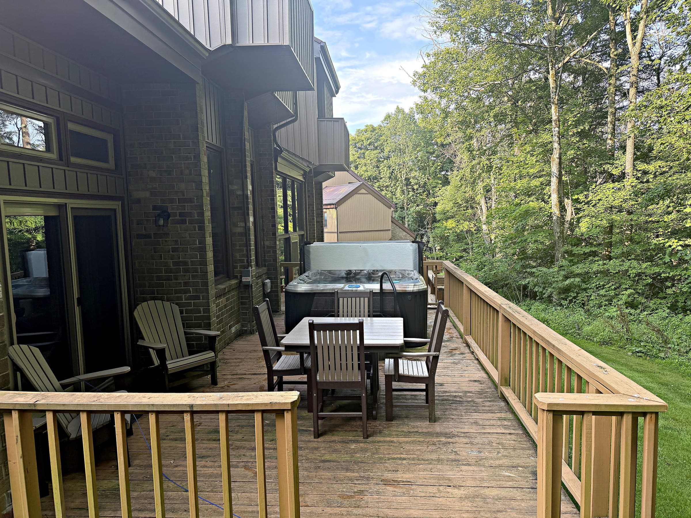 The back deck running the length of the house — hot tub, dining, and woods